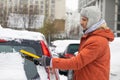 Young Caucasian man cleaning snow from car with brush. Transport, winter, people and vehicle concept. Royalty Free Stock Photo