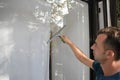 A young man cleans and polishes windows with a sponge