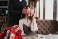 A young man closes his eyes to the girl, his wife, and gives a bouquet of red flowers in a cafe by the window. Royalty Free Stock Photo