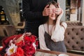 A young man closes his eyes to the girl, his wife, and gives a bouquet of red flowers in a cafe by the window. Royalty Free Stock Photo