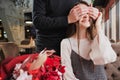 A young man closes his eyes to the girl, his wife, and gives a bouquet of red flowers in a cafe by the window. Royalty Free Stock Photo