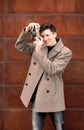 The young man in a coat photographs model the vintage camera at a metal rusty wall