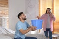 Young man collecting leaking water from ceiling while his girlfriend calling roof repair service Royalty Free Stock Photo