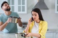 Young man collecting leaking water from ceiling while his girlfriend calling roof repair service in kitchen Royalty Free Stock Photo