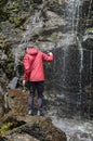 Young man collects water in a thermos of a waterfall