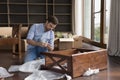 Young man collects wooden nightstand on relocation day