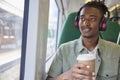 Young Man Commuting To Work Sitting On Train Wearing Wireless Headphones With Takeaway Coffee Royalty Free Stock Photo