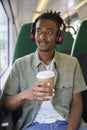 Young Man Commuting To Work Sitting On Train Wearing Wireless Headphones With Takeaway Coffee Royalty Free Stock Photo