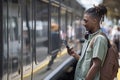 Young Man Commuting To Work On Train Standing On Platform Looking At Mobile Phone As Train Arrives