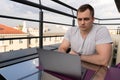 Young man connecting with a laptop at the cafe. Town buildings on background Royalty Free Stock Photo