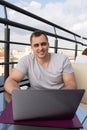 Young man connecting with a laptop at the cafe. Town buildings on background Royalty Free Stock Photo