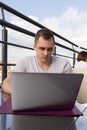 Young man connecting with a laptop at the cafe. Town buildings on background Royalty Free Stock Photo