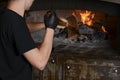 Young man cooking food in a professional stone oven with red fire inside the oven. Professional cook in a restaurant.
