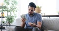 Young man counting and distributing money while sitting on sofa