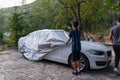 Young man covers his car with a car cover in the street