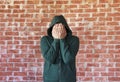 Young man covers his face with hands with bricks wall as background Royalty Free Stock Photo