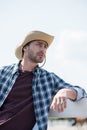 Young man in cowboy hat and checkered shirt looking away and leaning on fence at ranch Royalty Free Stock Photo
