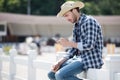 Young man in cowboy hat using smartphone while sitting on wooden fence Royalty Free Stock Photo