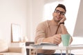 Young man with cup of drink relaxing at table in office Royalty Free Stock Photo