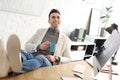 Young man with cup of drink relaxing at table in office Royalty Free Stock Photo