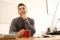 Young man with cup of drink relaxing at table in office Royalty Free Stock Photo