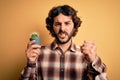 Young man with curly hair and beard holding small cactus plant pot over yellow background annoyed and frustrated shouting with Royalty Free Stock Photo