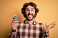 Young man with curly hair and beard holding small cactus plant pot over yellow background very happy and excited, winner Royalty Free Stock Photo