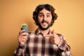 Young man with curly hair and beard holding small cactus plant pot over yellow background very happy pointing with hand and finger Royalty Free Stock Photo