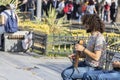 Young man with curly hair on the street is singing with a violin instrument. He sits on the bench. People give money