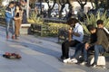 Young man with curly hair on the street is singing with a violin instrument. He sits on the bench. People give money