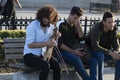 Young man with curly hair on the street is singing with a violin instrument. He sits on the bench. People give money