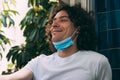 A young man with curly long hair, with a medical mask removed from his face, closed his eyes and smiles. Royalty Free Stock Photo