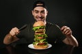 Young man with cutlery eating huge burger