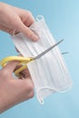 Young man cuts a medical protective mask with yellow scissors on a blue background before throwing it away