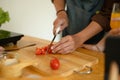Young man cutting tomato on wooden board at kitchen counter. Closeup view Royalty Free Stock Photo