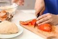 Young man cutting tomato on wooden board in kitchen Royalty Free Stock Photo