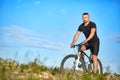 Young man cycling on a green meadow against blue sky with clouds. Royalty Free Stock Photo