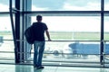 Young man is standing near window at the airport and watching pl Royalty Free Stock Photo