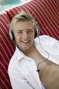 Young man on deckchair by pool listening to music on headphones portrait Royalty Free Stock Photo
