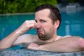 Young man with disgust on his face pinches nose, something stinks, very bad smell in swimming pool because of chloride.