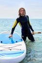 young man in diving suit spedting time at sea, carrying surfboard and paddle Royalty Free Stock Photo
