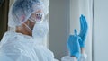 Young man doctor male nurse medical worker in special protective suit uniform with glasses and cap puts on rubber blue Royalty Free Stock Photo