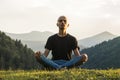 Young man does yoga in mountains at sunset