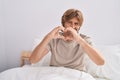 Young man doing heart gesture sitting on bed at bedroom Royalty Free Stock Photo