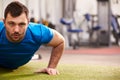 Young man doing push ups at a gym, looking to camera, copy space