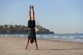 Young man doing yoga exercise - handstand on sandy beach near the sea. Active lifestyle concept. Royalty Free Stock Photo