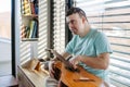 Young man with down syndrome playing acoustic guitar, sitting by window, holding and strumming guitar, making music. Royalty Free Stock Photo