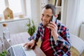 Young man with Down syndrome sitting at desk in office and using smartphone and laptop, looking at camera and smiling Royalty Free Stock Photo