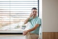 Young man with Down syndrome sitting by window, making phonecall with smartphone. Royalty Free Stock Photo