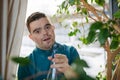 Young man with Down syndrome taking care of indoor plants, misting leaves with spray bottle.